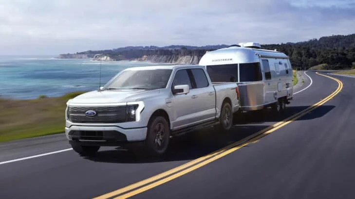 Vue commerciale du F150 Lightning électrique tirant une caravane, sur une route littorale.