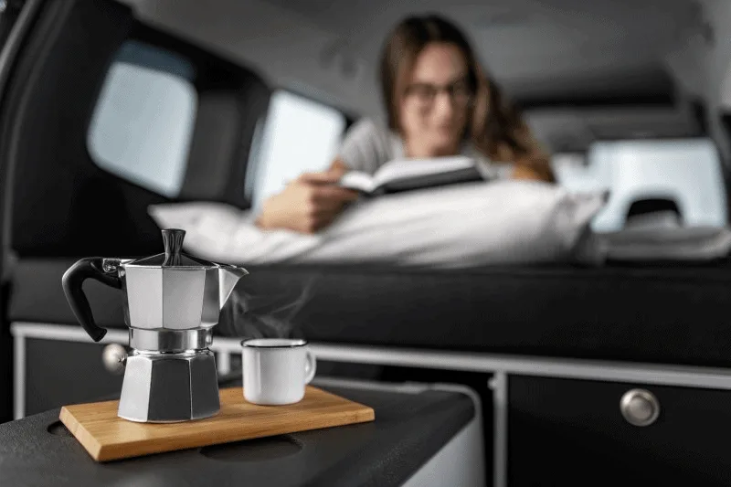 Photo présentant l'arrière d'un Citan transformé en intérieur cosy, avec banquette couchette et et café maison.