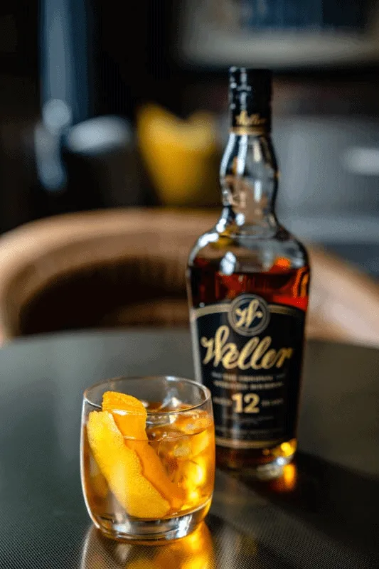 Bouteille de Weller, whiskey de 12 ans d'age, et un verre rempli et agrémenté de zestes de citron.