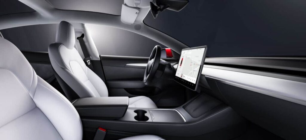 Photo montrant l'intérieur au design épuré de la Tesla Model 3, qui fait ressortir le volant et l'écran de conduite.