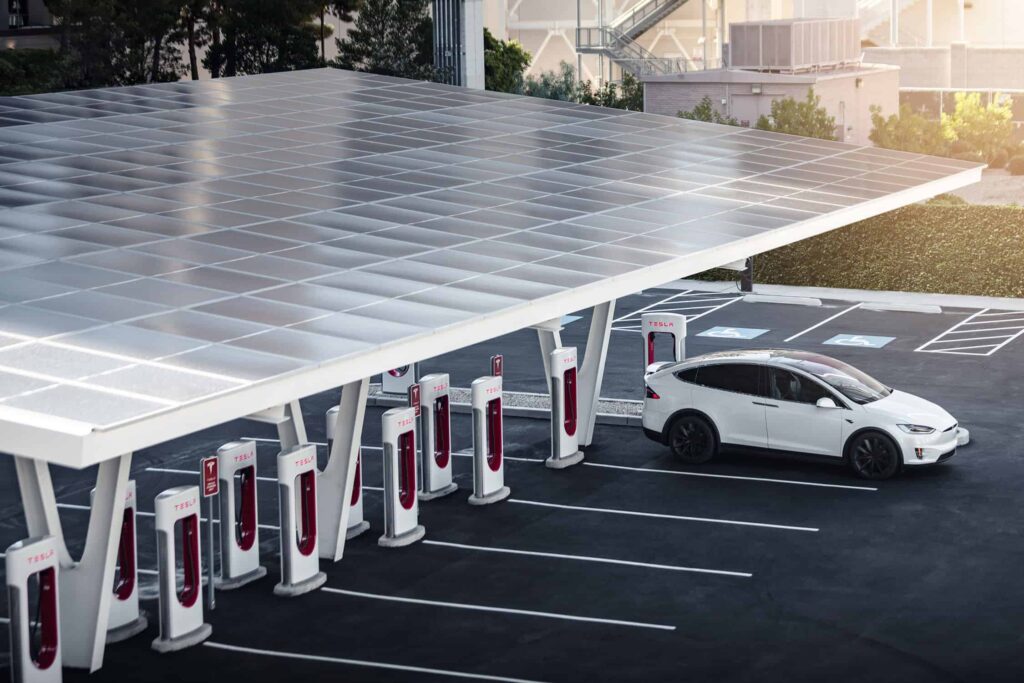 Tesla Model Y effectuant sa recharge à un superchargeur sous une ombrière équipée de panneaux solaires.