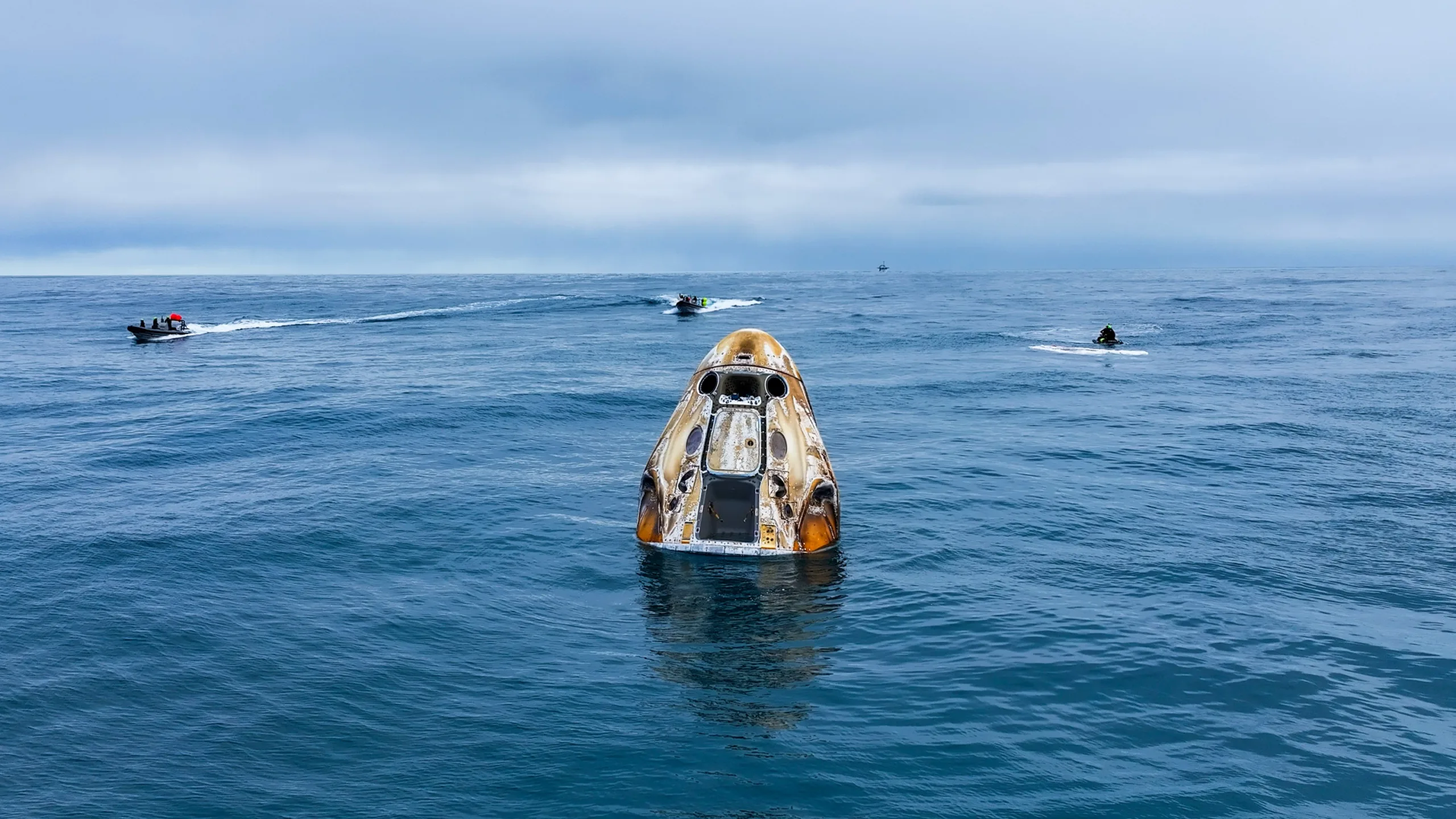Une capsule Dragon flottant après un amerrissage, entourée de bateaux de récupération