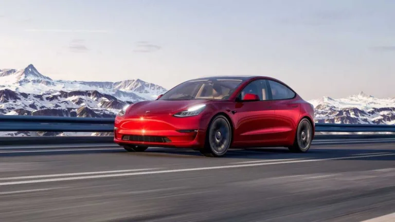 Tesla Model 3 rouge sur une route, montagnes enneigées en arrière-plan