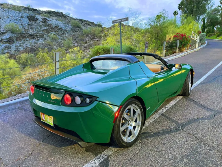 Tesla Roadster de première génération, vert, capote ouverte, sur une route de colline