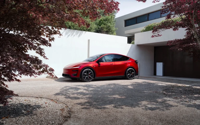 Un Tesla Model Y rouge branché à une borne de recharge devant une maison
