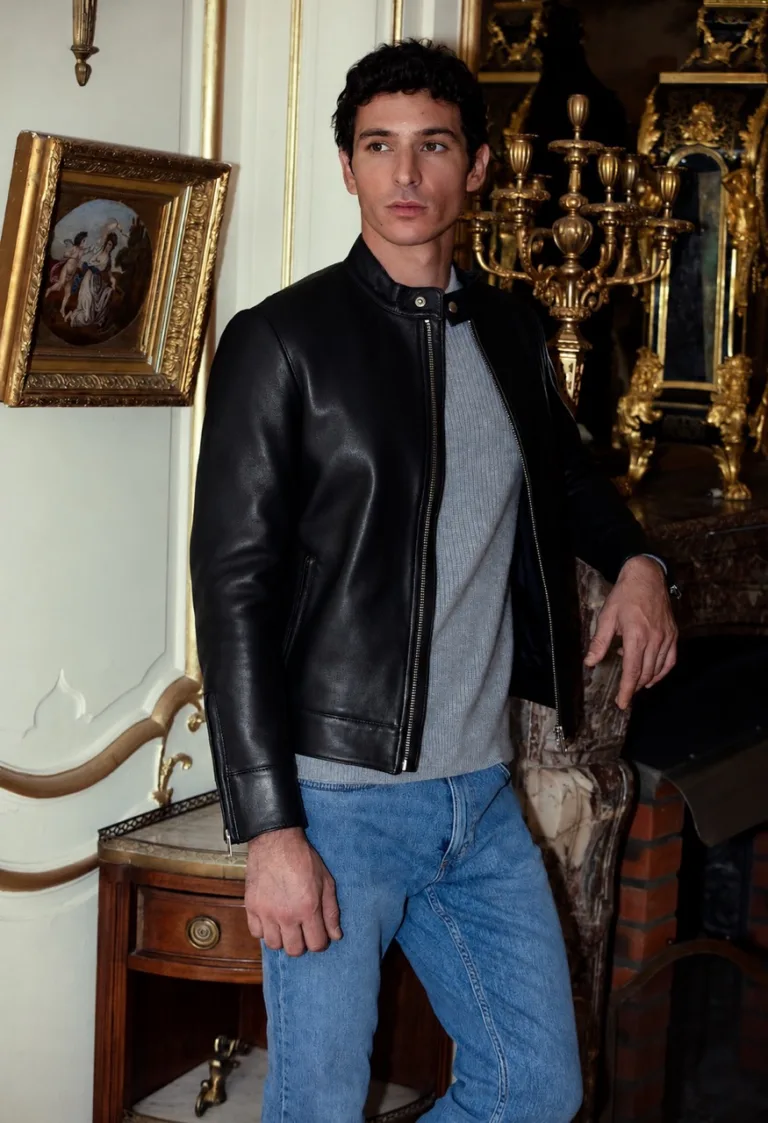 Un homme porte le Blouson Minimaliste en cuir noir d'Atelier Bertrand avec un pull gris et un jean