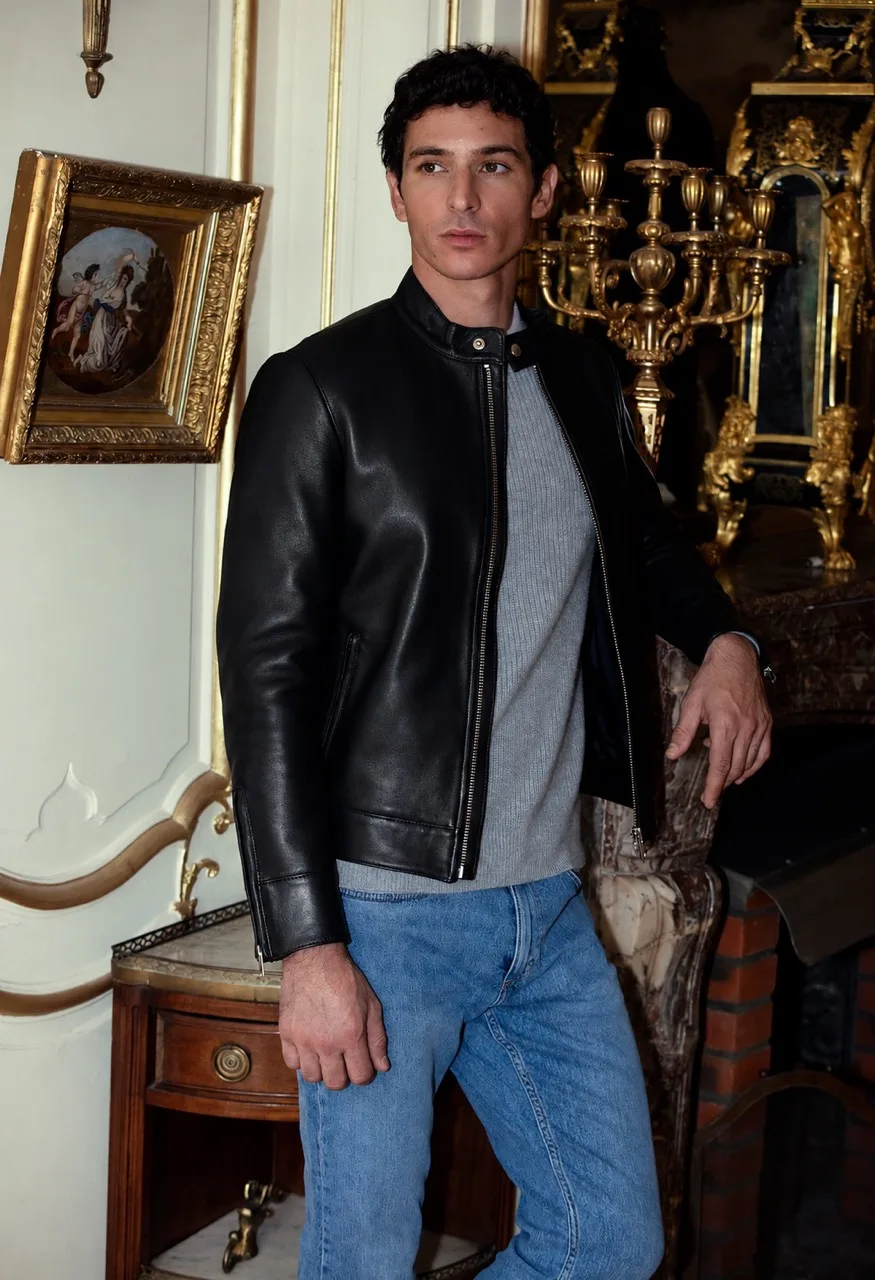 Un homme porte le Blouson Minimaliste en cuir noir d'Atelier Bertrand avec un pull gris et un jean