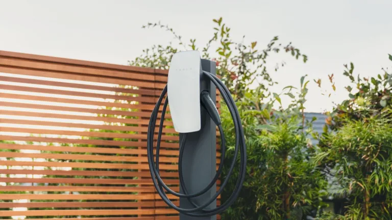 Borne de recharge Tesla Wall Connector fixée sur un pied, câble enroulé, devant une clôture en bois