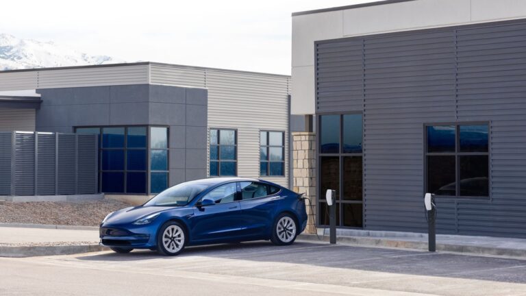 Tesla Model 3 bleue garée devant des bâtiments d’entreprise équipés de bornes de recharge sur pied
