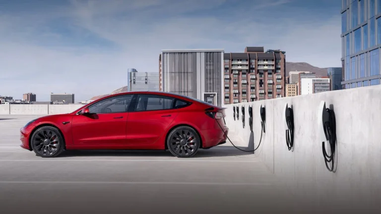 Tesla Model 3 rouge branchée à une rangée de bornes de recharge murales sur un parking en toiture