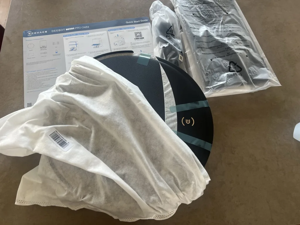 Le robot DEEBOT T90S sous sa housse, avec la notice et les accessoires