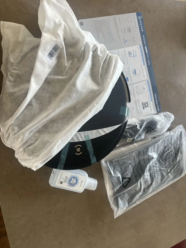 Le robot sous sa housse, la notice, les sacs d'accessoires et le flacon de détergent
