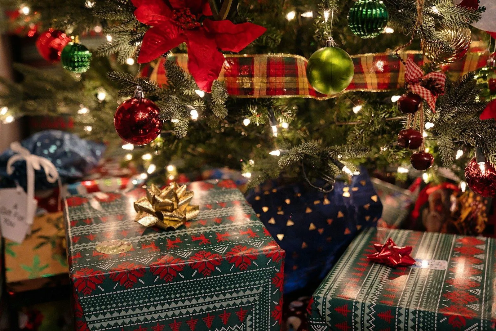 Cadeaux emballés sous un sapin de Noël décoré de boules rouges et vertes et de guirlandes lumineuses