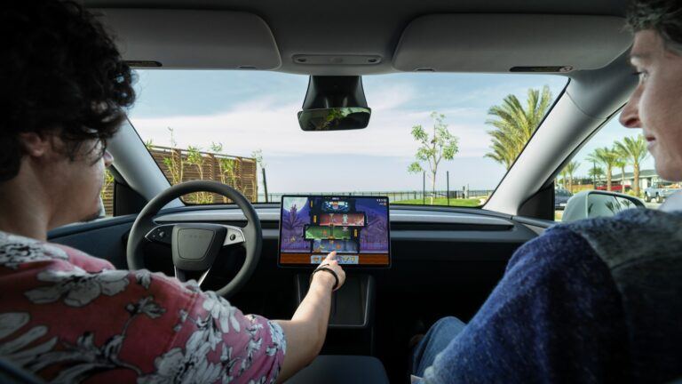 Deux occupants d’un Tesla Model Y à l’arrêt, une main touche l’écran tactile central