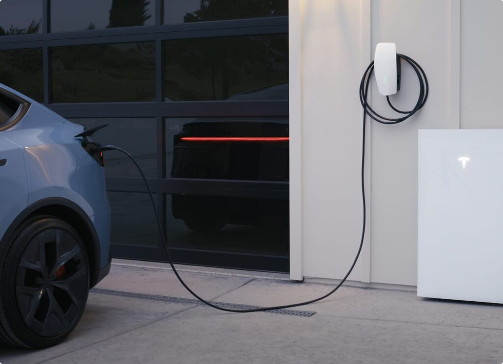 Un Model Y relié par son câble à un Wall Connector, à côté d’un Powerwall 3 blanc