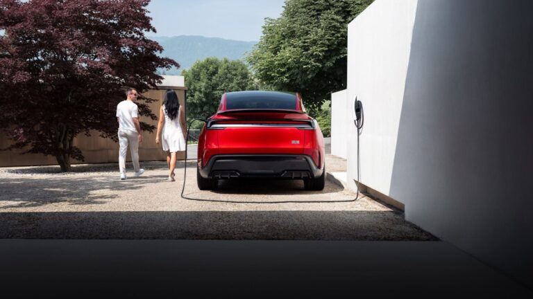 Model Y rouge garée devant une maison, branchée à un Wall Connector fixé au mur