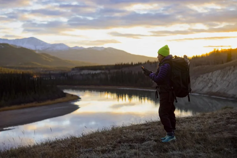 Une randonneuse consulte son téléphone au bord d'une rivière, loin de toute antenne : l'usage visé par Starlink Mobile