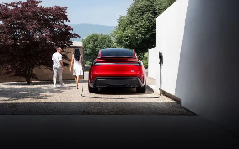 Une Tesla Model Y rouge branchée à son chargeur mural, devant une maison