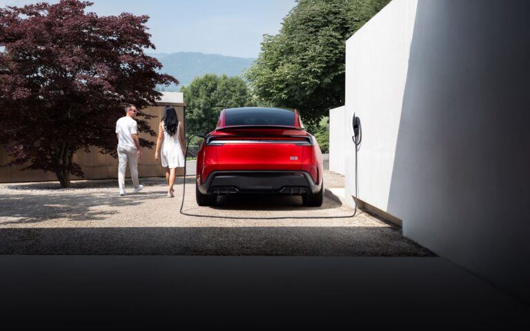 Une Tesla Model Y rouge branchée à son chargeur mural, devant une maison