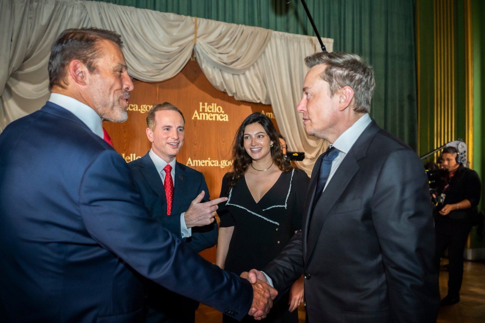 Tony Robbins et Elon Musk se serrent la main devant le décor « Hello America » du lancement d’America.gov, à Washington