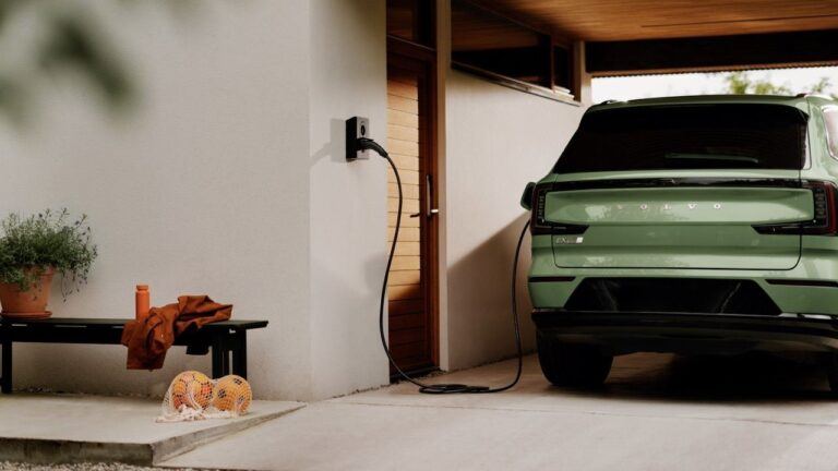 Borne Zaptec Go 2 fixée au mur blanc d’un abri de voiture, câble branché sur un SUV électrique vert